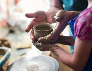 instructor helping child make a pottery piece